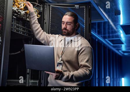 Young engineer touching cables and using laptop in server room Stock Photo