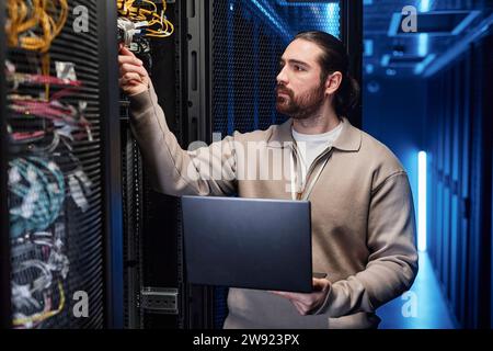 IT professional holding laptop and examining cables in server room Stock Photo