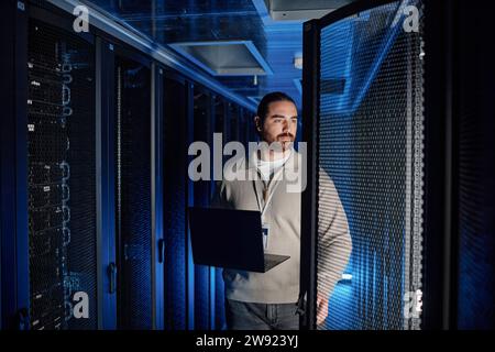 Engineer holding laptop and examining supercomputer in server room Stock Photo