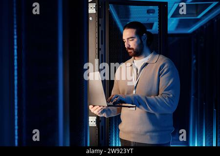 IT professional working on laptop and standing near server rack Stock Photo