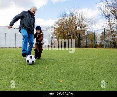 Grandson and grandfather having fun playing with ball at soccer field Stock Photo