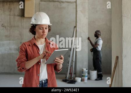 Young engineer using tablet PC with coworker in background at construction site Stock Photo