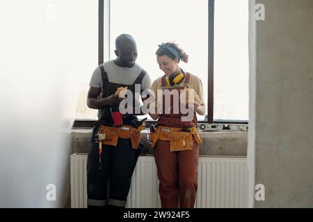 Smiling construction workers taking lunch break and using smart phone at site Stock Photo