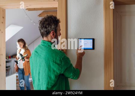 Man adjusting temperature through app on tablet PC in attic at home Stock Photo