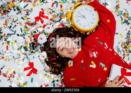 Happy girl lying on confetti with clock and gift boxes Stock Photo