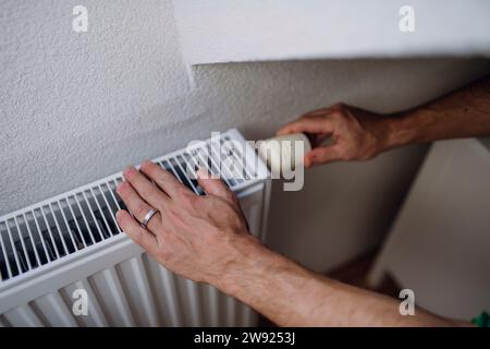 Man adjusting radiator with regulator near wall Stock Photo