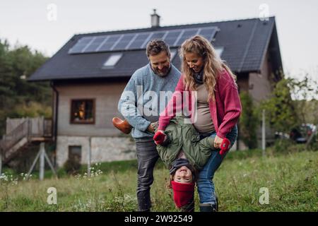 Smiling parents carrying daughter upside down in front of house Stock Photo