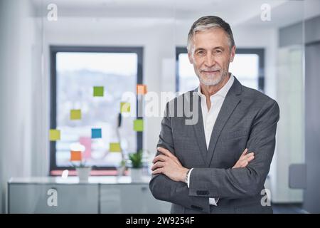 Smiling senior businessman standing with arms crossed Stock Photo