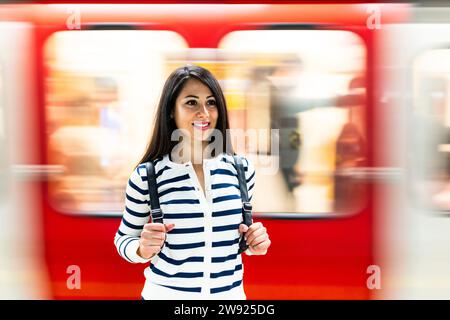 Happy woman with backpack standing in front of passing subway Stock Photo