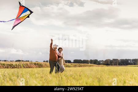 Happy senior couple flying kite in field on sunny day Stock Photo