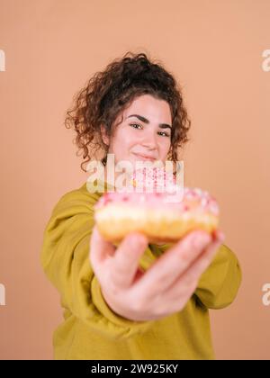 Young woman showing doughnut against peach background Stock Photo