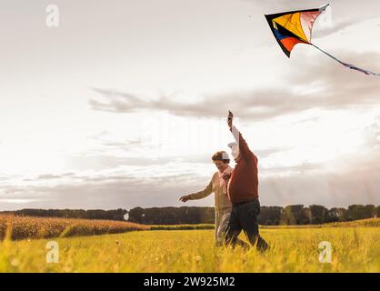 Happy senior couple running and flying kite in field on sunny day Stock Photo