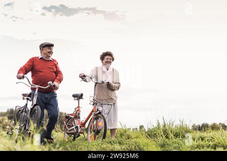 Happy senior couple walking with bicycles under sky Stock Photo