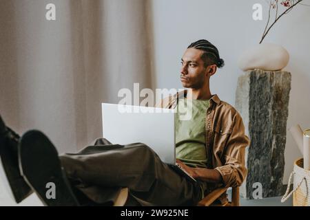 Thoughtful young man with laptop relaxing with feet on table at home Stock Photo