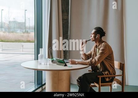 Thoughtful young man looking out through window sitting at table Stock Photo