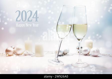 Happy New Year 2024 text, two champagne glasses toast, bright background with candles, Christmas baubles and snowy bokeh, selected focus, narrow depth Stock Photo