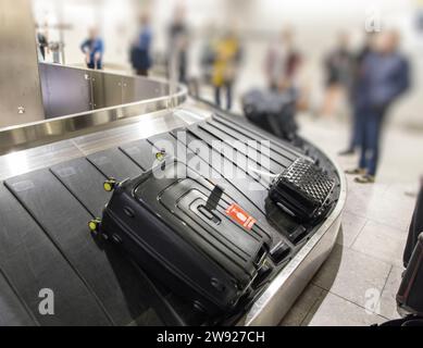 Luggage on airport baggage reclaim with passengers waiting to collect, Heathrow, London, UK Stock Photo