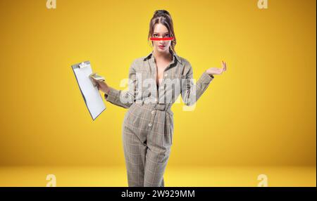 Charming woman in a suit stands in the studio on a yellow background. Coaching and mentoring concept. Mixed media Stock Photo