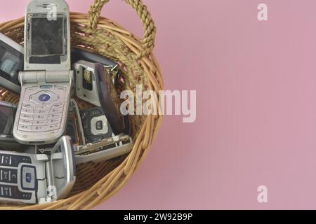 Old mobile phones spilling from a basket, set against a pink backdrop, poker cards and chips Stock Photo