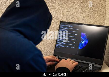 Man looked like hacker in a hood sitting in the front of laptop, writing a code Stock Photo