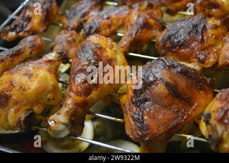 Deliciously fried pieces of marinated chicken on a metal mesh with a tray of vegetables like: potatoes, zucchini, red bell peppers, white onions, gree Stock Photo