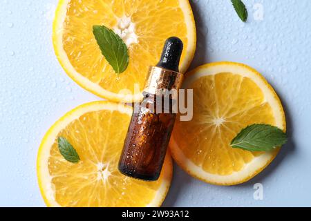 Bottle of cosmetic serum, orange slices and green leaves on light blue background, flat lay Stock Photo