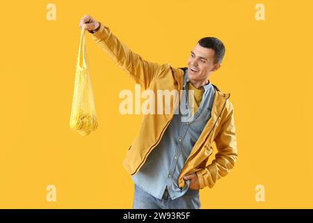 Young man holding string bag with lemons on yellow background Stock Photo
