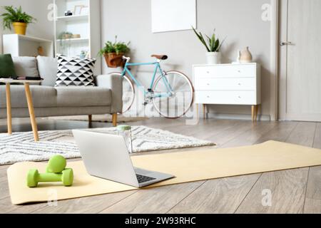 Laptop with dumbbells on fitness mat in living room Stock Photo