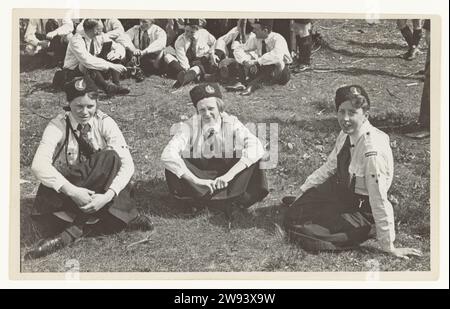 After the Procession Youth Storm, 1935 - 1937 photograph In a wooded area, three girls from the youth storm are on the ground in uniform, presumably after the parade. The stormster on the right has the word Amersfoort on her sleeve, the left is wearing nestles. There are some male members on the ground in the background. Zeist photographic support gelatin silver print military parade, pageant Zeist Stock Photo