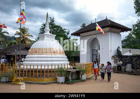 People walk past a small stupa adjacent to the western entrance gate to the Temple of the Sacred Tooth Relic at Kandy in Sri Lanka. Stock Photo