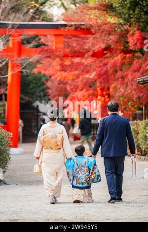 Back view a family wearing Japanese traditional kimono at a shrine during the autumn maple season. A red Torii gate in the background. Stock Photo