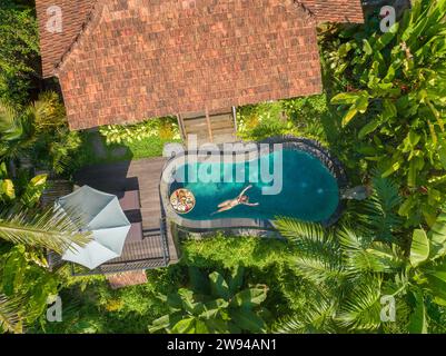 Aerial view of a young woman relaxing in a swimming pool, rural Bali ...