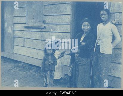 Javanese, Groote Combéweg, 1903 - 1910 photograph Two Javanese women and two girls standing in the door of a wooden house on the Grote Combéweg in Paramaribo. Part of the photo album Souvenir de Voyage (part 2), about the life of the Doijer family in and around the MA retreat plantation in Suriname in the years 1903-1910. Suriname photographic support cyanotype  Suriname. Paramaribo. Big Combéweg Stock Photo