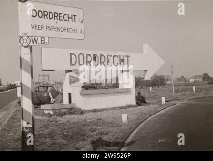 ANWB sign: Dordrecht, 1941 - 1942 photograph Along a motorway is an ANWB sign towards Dordrecht. In addition, a construction of stone with an arrow that contains the inscription: Dordrecht. Below a triangle with flying bird. Reference to Luftwaffe base? A German soldier leans against the construction. Behind it are two cars with a blond boy. Dordrecht photographic support gelatin silver print occupation  war Netherlands. Dordrecht Stock Photo