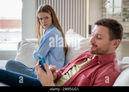 Marital discord, crisis in family relations caused by husband smartphone addiction, neglecting wife Stock Photo