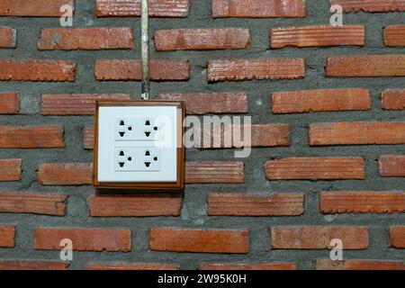 White socket is installed on orange brick wall in hotel or resort room. Stock Photo
