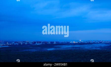 Dark storm clouds over the houses of the evening city after heavy rain with fog over the trees Stock Photo