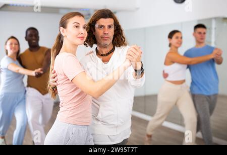 Smiling dancing people practicing movements while dancing in pairs in dance school for adults Stock Photo