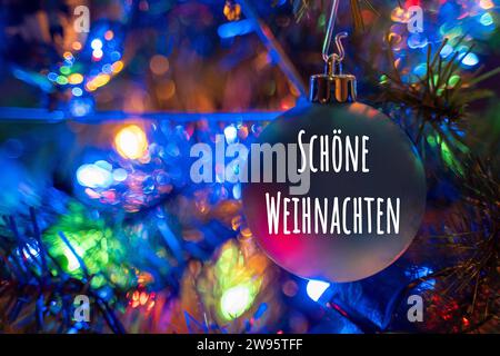 Kammlach, Bavaria, Germany - December 24, 2023: Merry Christmas greeting on a Christmas tree ball on a colorfully decorated Christmas tree. Christmas greeting FOTOMONTAGE *** Schöne Weihnachten Gruß auf einer Christbaumkugel an einem bunt geschmückten Weihnachtsbaum. Weihnachtsgruß FOTOMONTAGE Stock Photo
