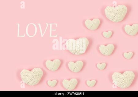 Many white knitted hearts with an inscription "love" on pink background. Concept of Valentine day. Greeting card for Valentine,  Mother day or birthda Stock Photo