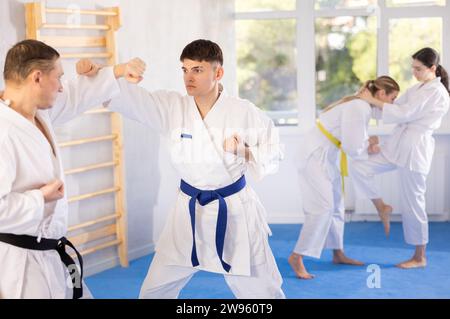 Young male attendee of karate classes fighting with middle-aged man in sports hall Stock Photo