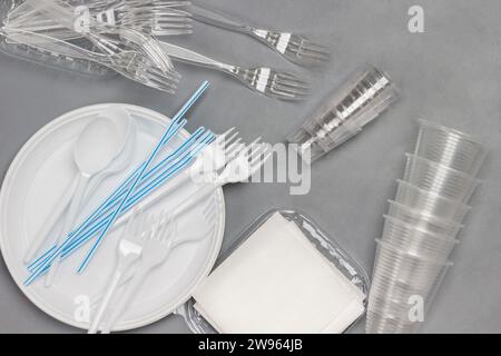 Disposable white plastic tableware. Plate, spoons, forks, straws for drinks. Plastic processing problem. Ecology environmental care. Flat lay. Grey ba Stock Photo