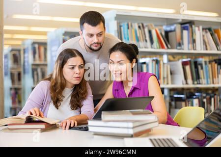 Group of positive friendly international university students working on joint research in library, looking for information in books and websites using Stock Photo