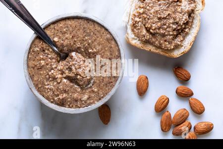 Almond butter in a bowl with almonds on a marble background Stock Photo