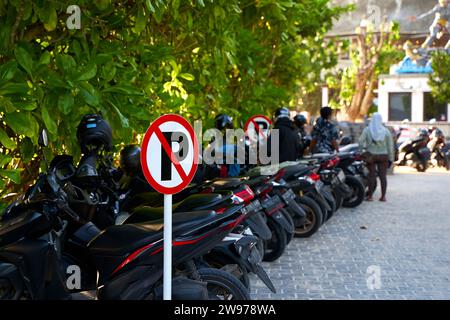 Warning sign - parking is prohibited. Full motorcycle parking near a no parking sign. Bali, Indonesia - 11.30.2022 Stock Photo