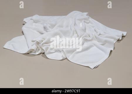 Used white towel is untidily lying on brown floor in hotel or resort room after guest's use in toilet or restroom when taking a shower. Stock Photo