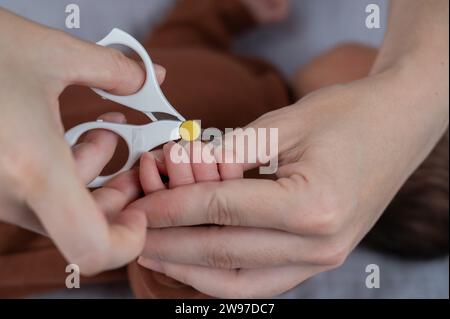 Mom cuts her newborn son's fingernails with small children's scissors. Stock Photo