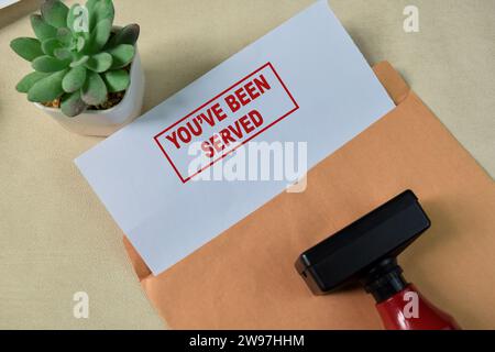 Red Handle Rubber Stamper and You've been served text above Brown envelope isolated on wooden background Stock Photo