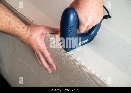 Worker stapling sofa lining with electric staple gun Stock Photo