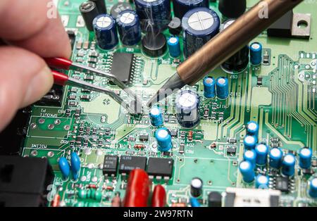 Close up of a technician's hands in a workshop. Repairer is soldering circuit board of electronic device on table with tweezers. Stock Photo